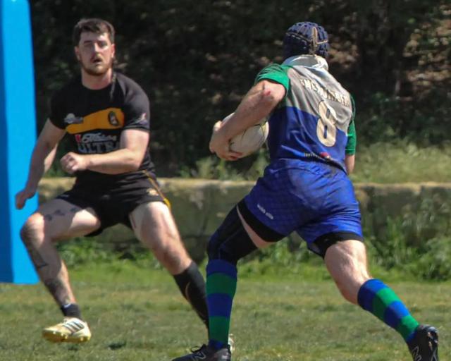 A Grunion player in the club's blue and green kit runs at a defender with the ball